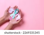 Small photo of Teal awareness ribbon with cervix shape on palms hand over pink background with copy space. Ovarian Cancer month, cervical cancer day.