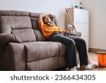 Tired Asian woman sitting on couch after cleaning the house