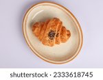 A croissant with black seeds on it on an oval plate on a white ground. Top shot
