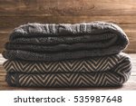A neat pile of knitted warm blanket: blue, gray, striped and white on a wooden background. Comfort, warmth and a homely atmosphere in the cold winter.