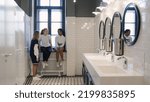 Small photo of Multiethnic teen girlfriends chat in school bathroom during break. Diverse teenage students gossip in campus toilet after lesson