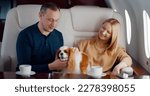 Small photo of Mature couple travelling in first class airplane with cute dog. Happy wealthy man and woman with cocker spaniel pet enjoying flight on luxurious private jet