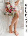 Small photo of The bride in a white negligee holds a gentle pink bouquet. Morning of the bride. Beautiful female feet.