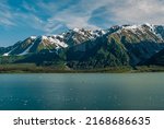 Small photo of Disenchantment Bay, Alaska, USA - July 21, 2011: Landscape, green forested mountain range with snow patches under blue cloudscape at entrance. Blue water with floating ice pieces.