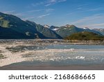 Small photo of Disenchantment Bay, Alaska, USA - July 21, 2011: Floating ice pieces on blueish water in front of green forested mountains and islet under blue cloudscape.