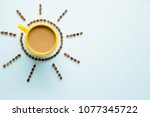 Yellow mug of coffee with milk on light pastel blue table from above. Wake up with morning coffee. Sun created from brown beans. Empty place for inspirational, motivational text or quote.  Top view.
