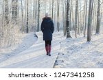 Young adult woman alone slowly walking on snow covered boardwalk after snowfall. Enjoying fresh air in park. Peaceful atmosphere in winter day.  Back view. 