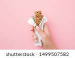 Young woman hand holding cereal bar on pastel pink table. Opened white pack. Closeup. Sweet healthy food.