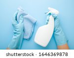 Hands in rubber protective gloves holding white spray bottle and rag. Detergent for different surfaces in kitchen, bathroom and other rooms. Closeup. Light pastel blue background. Point of view shot.