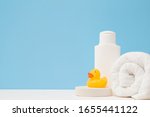 Small photo of White shampoo bottle, towel and wisp. Yellow rubber duck. Body washing concept. Closeup. Front view. Empty place for text or logo on light blue background. Pastel color.