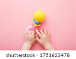 Baby girl hands playing with colorful rattle on light pink floor background. Pastel color. Closeup. Toys of development for infant. Point of view shot.