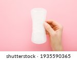 Young adult woman hand holding new white panty liner on light pink table background. Pastel color. Closeup. Female daily hygiene.
