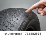 Man's hand finger pointing to the old, damaged and worn black tire tread. Change time. Tire tread problems and solutions concept.