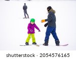 Small photo of Snowboard Winter Sport. little girl learning to snowboard, wearing warm winter clothes. Winter background.