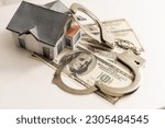 Small photo of iron handcuffs, a house made of on a background of American dollar bills. illegal sale of property. swindle. economic crimes.