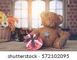 Teddy bear with a gift box on a wooden floor With flowers and windows in the background.