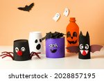 Small photo of DIY for kids. Halloween home activities. Handmade toys cute monster, bat, ghost and pumpkin. Reuse concept art from tin can, toilet tube, plastic bottle.