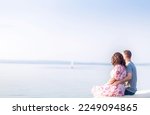 A young couple, a guy and a girl, are sitting on the shore of the lake and looking into the distance. Couple in love, valentine's day. Horizontal photo