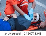 Small photo of Injured man on patient transport stretcher. Ambulance staff member assisting injured person with transport stretcher. Paramedics assisting injured person first aid on road