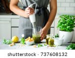 Woman using hand blender to make pesto. White kitchen interior design. Copy space. Vegetarian, clean eating lifestyle concept