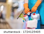 A bucket of cleaning products in hands with rubber gloves on a blurred background.