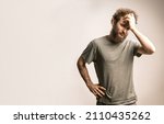 Small photo of Young guy holding his head in a pensive pose. Model with a beard ponders problems and solutions. Concept of fear, pessimism, emptiness, frailty, abandonment, uselessness. Copy Space