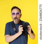 Small photo of Passionate old photographer beams with excitement, holding mirrorless photo camera, in isolated studio shot on yellow background. Seasoned photographer continues pursue photography passion with zeal
