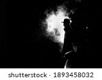 dramatic silhouette of a dangerous man in a hat at night in the rain in the city in the old crime 