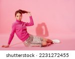 Fashionable redhead girl wearing trendy pink cashmere turtleneck sweater, sequin skirt, stylish white high top sneakers. Full-length studio portrait. Copy, empty space for text
