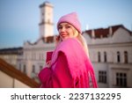 Happy smiling fashionable woman wearing trendy total pink outfit with knitted beanie hat, woolen fringed scarf, coat, posing outdoor. Copy, empty space for text