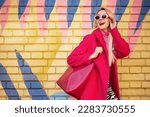 Fashionable happy smiling blonde woman wearing trendy pink sunglasses, fuchsia color coat, with faux leather tote, shopper bag, posing on colorful background. Copy, empty space for text
