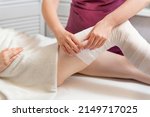 Small photo of Beautician wraps body of woman in white bandage. Cosmetologist wraps the leg of the customer. Body shaping