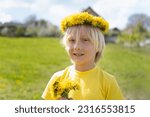 Small photo of Towheaded boy wears wreath of flowers and holds bouquet of dandelions standing in meadow. Summer vacation time