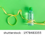 Small photo of A bottle of still water and a measuring tape on a green background. The concept of losing weight, healthy lifestyle, fasting. Drinking regime during exercise, sports. Duncan's diet. World Obesity Day.