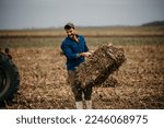Small photo of Good looking hard working man wearing boots and a shirt grabs a hay bale stacked in the western barn.