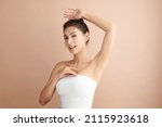 Small photo of Beautiful Young Asian woman lifting hands up to show off clean and hygienic armpits or underarms on beige background, Smooth armpit cleanliness and protection concept.
