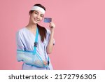 Small photo of Beautiful young asian woman wearing patient gown and soft splint due to sore arm show credit card on pink background, personal accident concept.