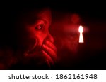 woman in the dark room looks into the keyhole glowing with red mysterious light. She covers her mouth to keep from screaming or being surprised or embarrassment.