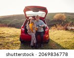 Loving couple chilling in car trunk by autumn lake drinking tea from vacuum flask. Man and woman travel by auto. Young people enjoy fall activities