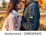 Small photo of Close up of couple holding hands. Sad woman hugging husband in ukrainian military uniform with flag chevron. Upset patriotic couple outdoors. Back from war