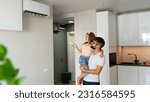 Small photo of Father with little daughter on hands turn on air conditioner using remote control. Happy family adjust comfortable temperature of cooler system