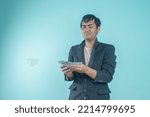 Small photo of Successful Asian businessman wearing black suit looking at his meager money with sad expression standing on blue background
