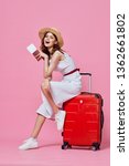 Small photo of A woman sits on a red suitcase with her leg bent over and holds tickets for a trip