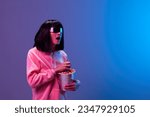 Small photo of Shocked adorable brunet woman in pink hoodie trendy specular sunglasses with popcorn open mouth look aside posing isolated in blue violet color light background. Neon party Cinema concept. Copy space