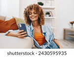 Small photo of Casual Sofa Chatter: Young Woman Holding Phone with a Smile in Cozy Living Room