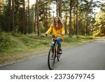 Small photo of Smiling woman on a bicycle in an autumn park. Beautiful female tourist rides a bicycle, enjoys the sunny warm weather. Lifestyle, weekend concept.