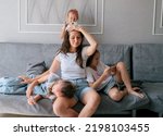 Tired young mother sits on couch and holds her head while her three naughty daughters play games on smartphones. lifestyle family together portrait.