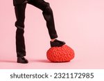 Small photo of Male feet trample the human brain model on a pink background. Hack the brain concept.