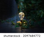 A decorative luminous lamp illuminates the foliage in the garden with a dim light at night. Warm cozy atmosphere of a summer evening