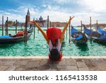 Happy traveller woman sits in front of the traditional gondolas of St. Mark's Square in Venice, Italy